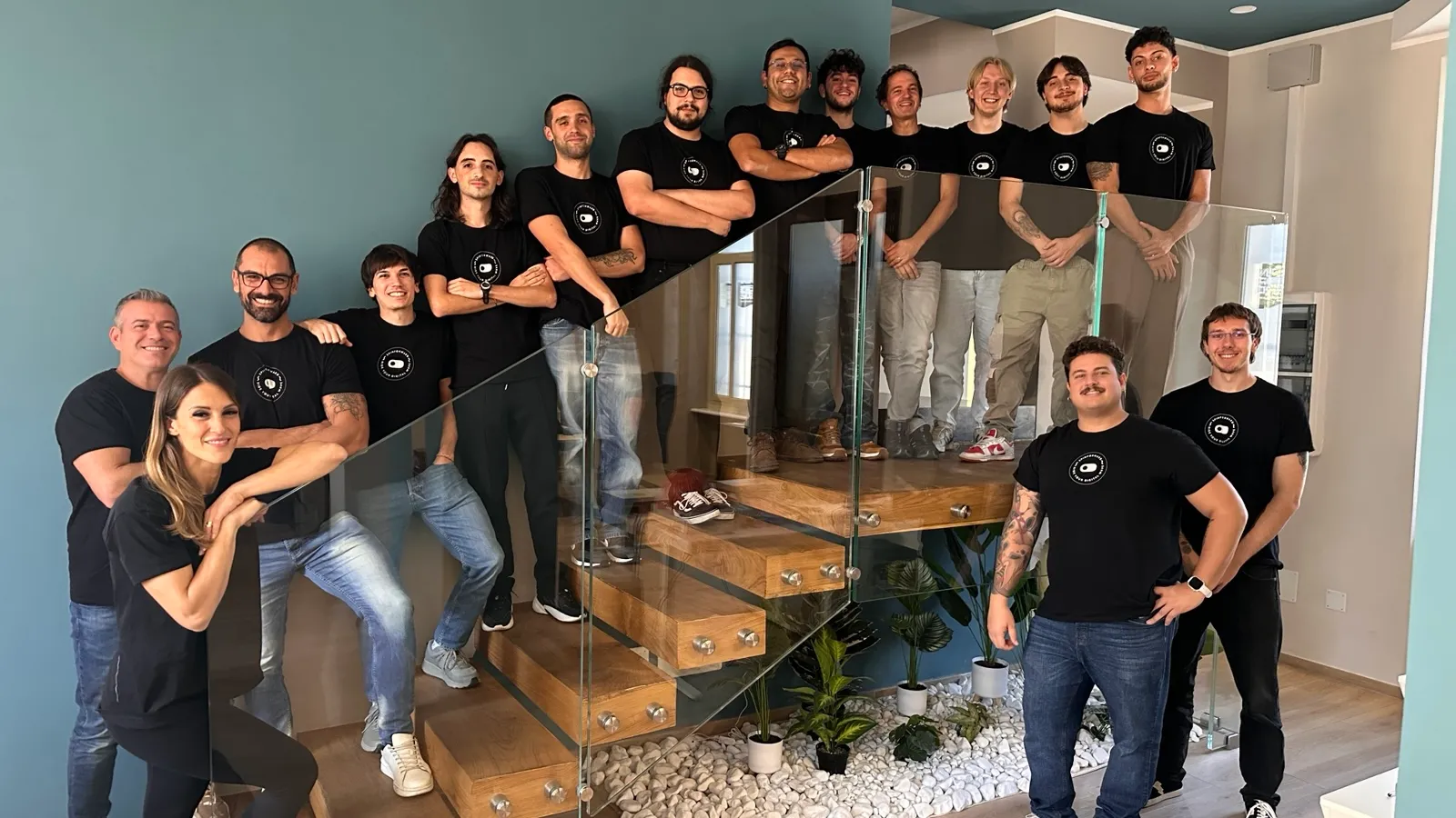 Il team Spinforward con la maglietta nera dell'azienda, in posa sulla scala di vetro e legno dell'ufficio.